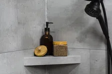 Thumbnail for Modern shower corner with black showerhead and natural skincare containers on grey stone shelf.