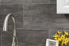 Thumbnail for Modern kitchen faucet on granite countertop with dark tile backsplash and decorative items including framed coffee quote and yellow flowers.