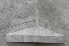 Thumbnail for Concrete triangular floating corner shelf mounted on textured gray concrete walls in an industrial style.