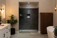 Thumbnail for Modern bathroom with white vanity, freestanding tub, dark tile shower, wooden cabinet, and ambient lighting.