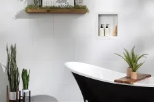 Thumbnail for Modern bathroom with black clawfoot bathtub, white tiled walls, plants, and decorative shelf with framed sign.