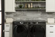 Thumbnail for Modern laundry room with black Samsung washer and dryer, white cabinets, decorative shelves, and gray tile wall.