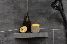Thumbnail for Modern shower corner with dark gray tiles, black showerhead, amber soap dispenser, and scrub jar with wooden lids.