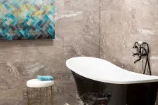 Thumbnail for Elegant black clawfoot bathtub with vintage faucet in modern beige tiled bathroom with abstract wall art and stool.