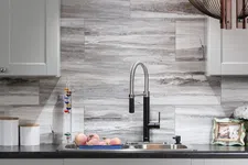 Thumbnail for Modern kitchen sink with black faucet, marble backsplash, peaches in blue tray, and decorative jars on countertop.