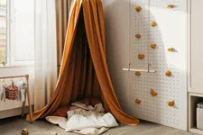 Thumbnail for Cozy children's playroom with an orange canopy tent, climbing wall, swing, and soft cushions near window.