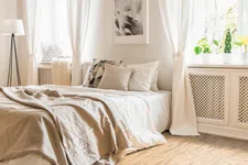Thumbnail for Bright modern bedroom with beige linen bedspread, white curtains, potted plants, and cork flooring in natural light.