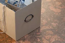 Thumbnail for Beige storage box holding a teddy bear, fabric sailboat, and cloth on textured brown floor.