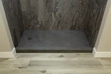 Thumbnail for Modern shower area with dark marble tiles and a gray stone shower base against light hardwood floor.