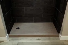 Thumbnail for Minimalist shower base with dark wall tiles and light wood flooring in a modern bathroom setup
