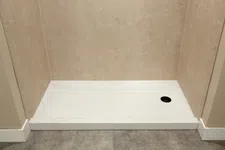 Thumbnail for Minimalist shower base with beige tiled walls and gray stone floor featuring a circular black drain.