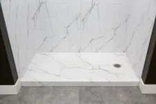 Thumbnail for White marble shower area with veined tiles, a built-in drain, and gray textured floor outside the shower