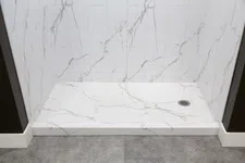 Thumbnail for Modern shower area with white marble tile walls and matching floor, featuring a metal drain and gray surrounding floor.