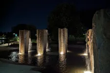 Thumbnail for Illuminated stone pillars with cascading water in a nighttime outdoor fountain surrounded by trees and pathways.