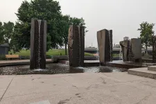 Thumbnail for Modern stone pillars with waterfalls in a park fountain surrounded by trees and benches on a cloudy day
