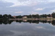 Thumbnail for Calm lake reflecting trees and houses under a cloudy sky during evening light.