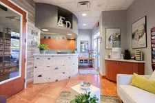 Thumbnail for Modern dental office reception area with curved desk, smiling posters, seating, and water station under bright lighting.