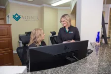 Thumbnail for Two female dental office staff smiling and interacting behind a reception desk at Volner Family Dental.