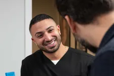 Thumbnail for Smiling male healthcare professional in black scrubs talking with a patient across a desk in a medical office.