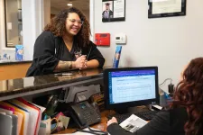 Thumbnail for Smiling woman with curly hair talks to receptionist at office counter with computer and phone.