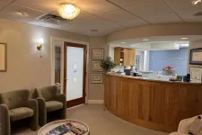 Thumbnail for Modern dental office reception area with wooden desk, comfortable chairs, and framed certificates on the wall.