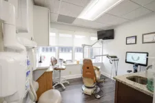Thumbnail for Modern dental office with brown dental chair, computer monitor, stool, and large windows letting in natural light.