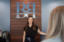Thumbnail for Smiling woman in black uniform standing in front of wooden wall with silver RRH logo in office setting