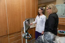Thumbnail for Female dentist in white coat showing patient dental imaging on a screen in a modern dental office