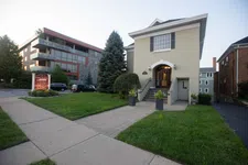 Thumbnail for Two-story beige building with stairs, green lawn, sidewalk, trees, and modern apartment in the background.