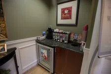 Thumbnail for Small coffee station with espresso machine, condiment dispensers, cups, and mini fridge in corner of room.