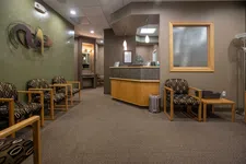 Thumbnail for Modern waiting room with patterned chairs, wooden tables, reception desk, and neutral beige walls.