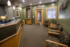 Thumbnail for Modern medical office waiting room with patterned chairs, reception desk, and potted plants under warm lighting.