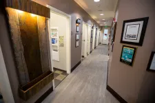 Thumbnail for Well-lit dental office hallway with open patient rooms and framed awards on beige walls.