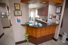 Thumbnail for Reception desk area with wood paneling, granite countertop, certificates on beige walls, and office supplies in dental clinic.