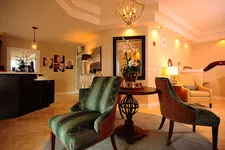 Thumbnail for Cozy waiting area with green upholstered chairs, wooden table, soft lighting, and warm beige walls in a modern interior.