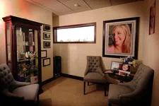 Thumbnail for Cozy waiting room with tufted chairs, framed portraits, a glass display cabinet, and wall certificates.