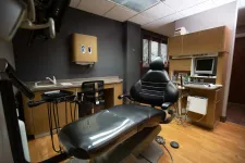 Thumbnail for Modern dental office with black dental chair, cabinetry, computer monitor, and medical equipment on wood floor.