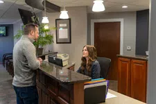 Thumbnail for Man in gray sweater talking to receptionist at office front desk with computer and files