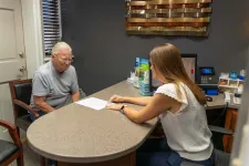 Thumbnail for Older man consulting with a female professional at a desk in an office setting with documents and computer.