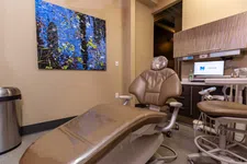 Thumbnail for Modern dental exam room with brown chair, computer screen, artwork, and dental equipment in beige tones.