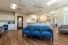 Thumbnail for Bright medical office waiting room with blue chairs, wooden floor, reception desk, and large windows.