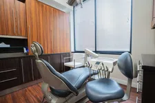 Thumbnail for Modern dental clinic room with dental chair, equipment, wooden cabinets, and large window with blinds.