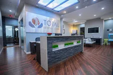 Thumbnail for Modern dental office reception area with wood flooring, stone front desk, and Total Dental Care signage.