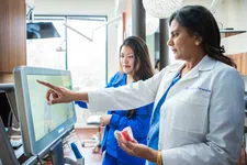 Thumbnail for Female dentist in white coat showing dental model and pointing at screen with assistant in clinic.