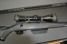 Thumbnail for Black hunting rifle with a mounted scope inside a protective foam case on a textured surface.