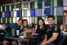 Thumbnail for Four friends smiling together at a bustling café, enjoying drinks and each other's company.