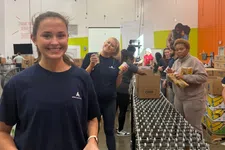 Thumbnail for Volunteers packing canned food items on a conveyor belt in a busy warehouse setting