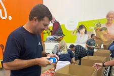 Thumbnail for Volunteers packing food items into CSFP boxes at a warehouse with a mural in the background.