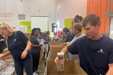 Thumbnail for Volunteers packing food boxes with pasta and canned goods at a community food bank warehouse.