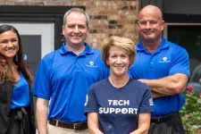 Thumbnail for Smiling diverse tech support team standing outside office building in branded blue shirts and business attire.